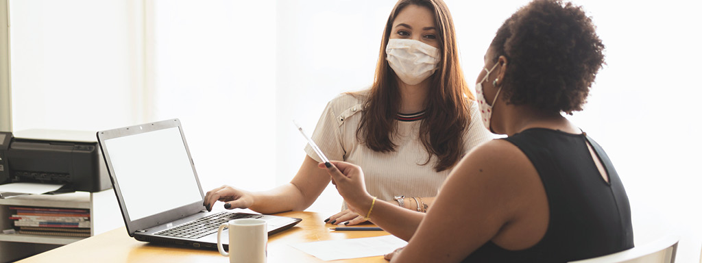 Two women wearing face masks reviewing information on a laptop